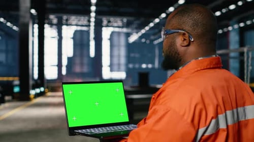 Green Screen Laptop with Black Technician Overseeing Fabrication Tasks