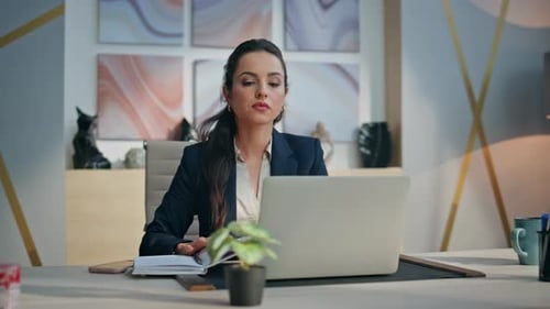 Woman Works at Desk Using Laptop and Notebook