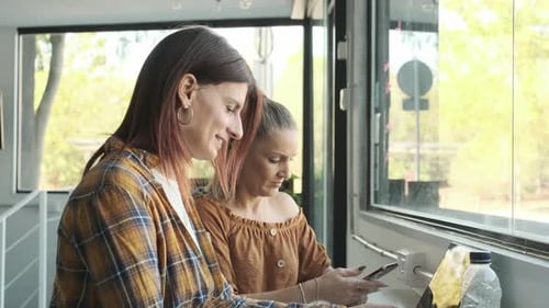 Women Using a Laptop and a Mobile Phone While Sitting in a Coffee Shop