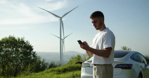 Young Man Charging Electric Car with Wind Turbines