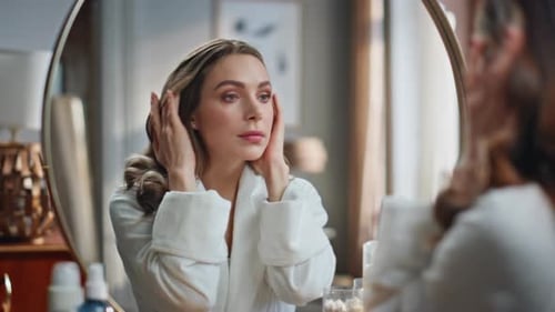 Woman Applies Lotion to Face in Mirror