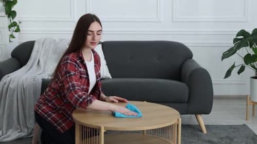 Woman wiping dust from wooden table indoors
