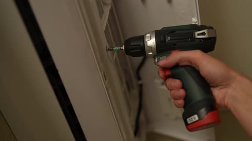 Hand of HVAC Technician Installing Air Conditioner Using Cordless Electric Screwdriver Performing