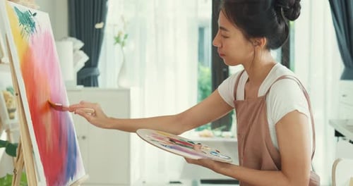 Asia Female use brush painting on canvas create artwork in cozy workshop at home.