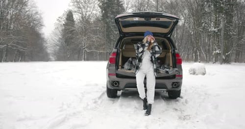Young Woman with Hot Drink Near Car at Winter Forest