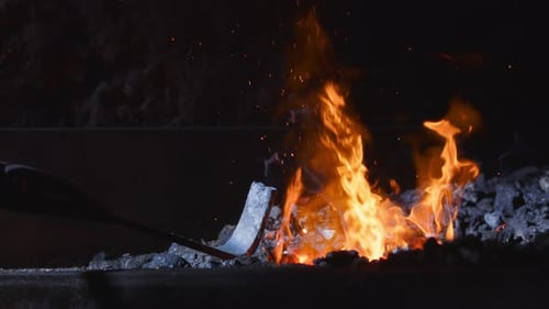 Embers rise as metal piece is inserted into swelteringly hot blacksmithing forge