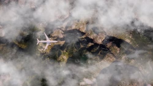 Vista aérea de un avión volando por encima de un escarpado terreno montañoso y nubes