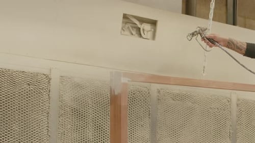 Maler beim Airbrush eines Holzrahmens mit weißer Farbe in einer großen Werkstatt in Zeitlupe