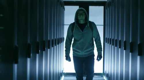 Serious Hacker Looks into Camera and Walks Through Data Center Corridor.