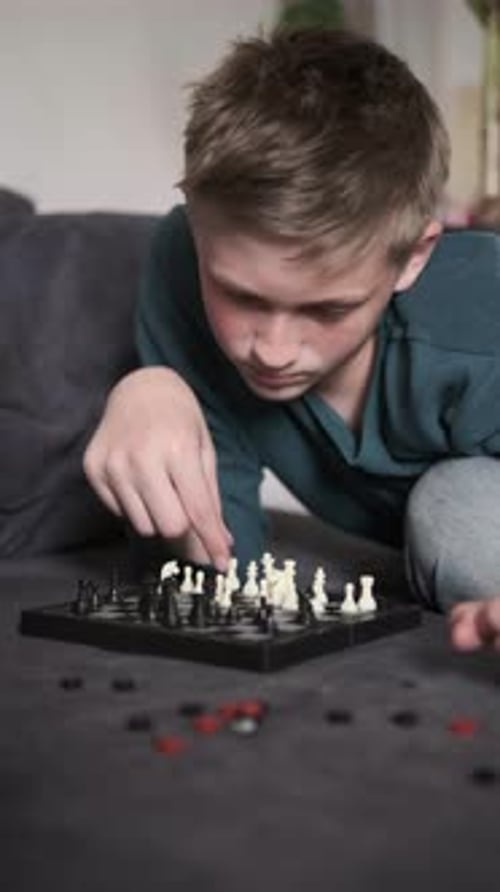 Teenage Boy Playing Chess Alone on Sofa Thinking Deeply Indoors