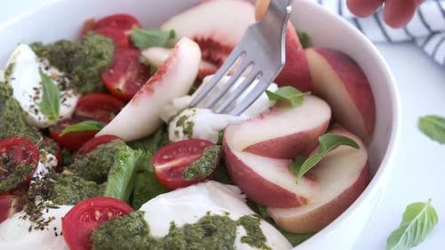 Making a fresh salad with mozzarella, peaches, and pesto