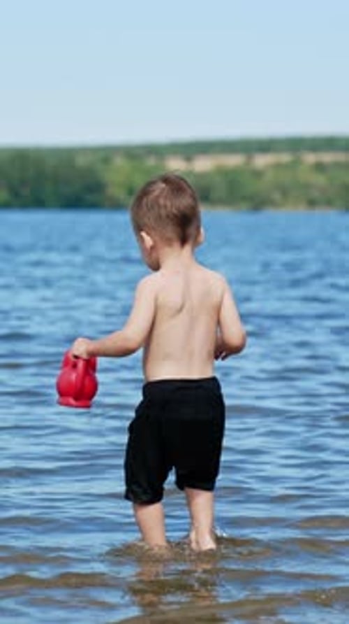 Summer sunny day and splashing on a beach. Small funny child playing on river with water.