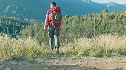 Man, hiking and looking with hand, field and view by lake, mountains and trekking in nature