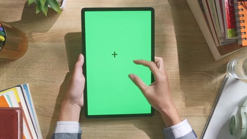 Top down view of man's hands using a green screen tablet on a wooden desk