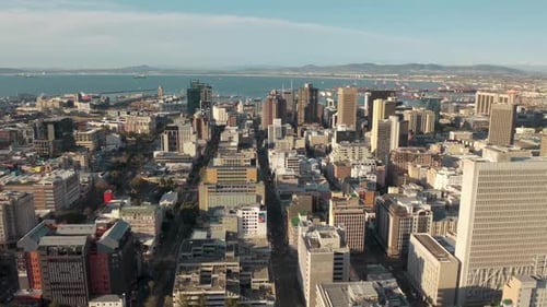 Aerial view of a cityscape with numerous buildings of varying heights, including high-rises. A harbo