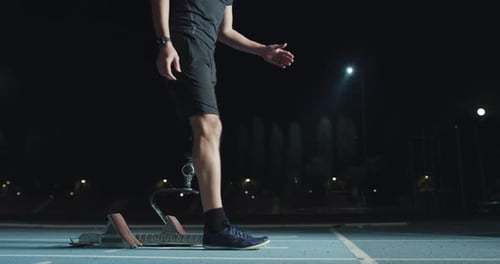 Athlete with Prosthetic Leg Using Starting Blocks at Night