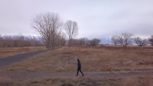 A man walks along a side trail towards a paved path - zoom out aerial