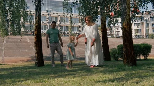 Little cute girl in green summer dress with parents in city park on a walk summer family lifestyle