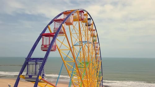 Aerial View of Around a Nonspinning Ferris Wheel in an Amusement Park with the Sea and Beach in the