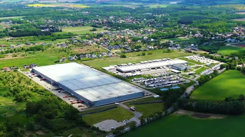 Semi truck with cargo trailer is travelling on a parking lot along a warehouse of a logistics park.