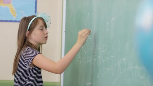 Elementary school student writes on chalkboard in diverse classroom