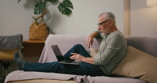Senior Man Using Laptop on Couch at Home