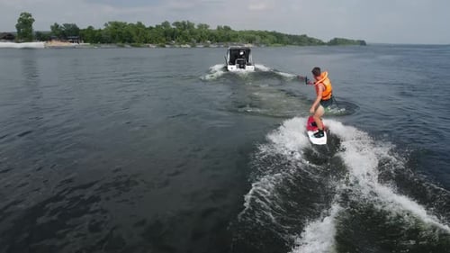 Ein junger Mann steht auf einem Wakeboard auf Ein Sportler reitet auf dem Wasser auf dem Brett Das Boot rollt weiter