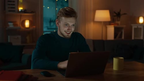 Handsome Smiling Man Works on a Laptop while Sitting at His Desk at Home, He Does Video Call and Ta