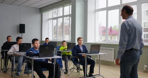 Lehrer mittleren Alters und Gruppe von Schülern im computergestützten Unterricht und Lernen