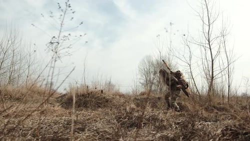 Camouflaged Person Walking Through Rural Terrain With Rifle