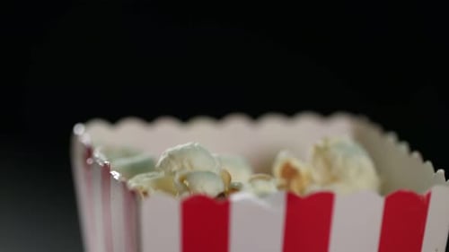 Full frame close-up: Plump fresh popcorn drops into small striped container