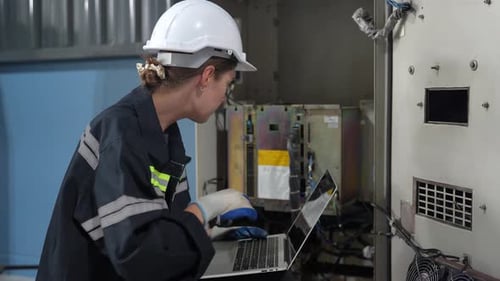 Une technicienne programme un bras robotique avec une tablette numérique et un robot d'assemblage dans une usine.