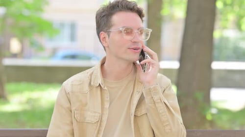 Young Adult Talking on Phone While Sitting on Bench