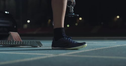 Cinematic close up shot of young runner with legs prosthesis prepares for launching off the start