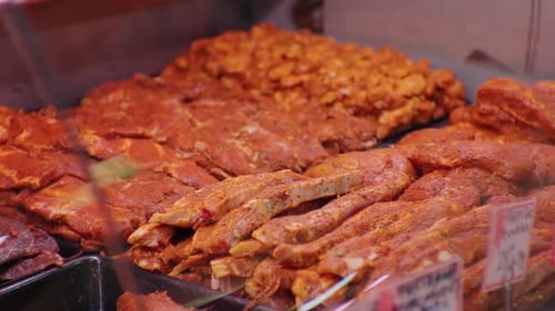 Large range of seasoned meat with spices and herbs in showcase in shop.