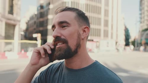 Close up, young man with beard talking on the phone on modern buildings background