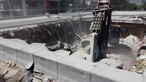 Primer plano de una excavadora que corta el techo de concreto restante creando polvo