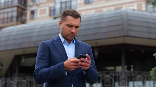 Portrait of Handsome Caucasian Male Walking in City While Using Smartphone