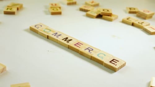 Wooden letters composing the word Commerce on an off white background with other scattered letters.