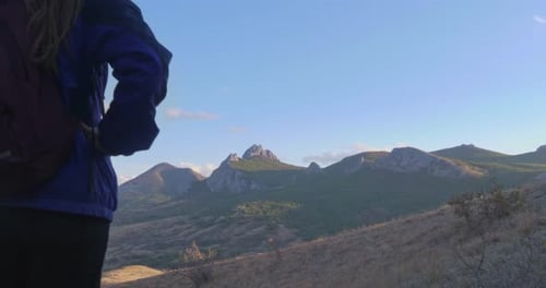 Rear View of a Young Adult Female Tourist with a Backpack Standing in the Rays of the Sunset in the