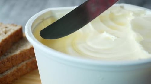Knife scooping spread from a tub with bread