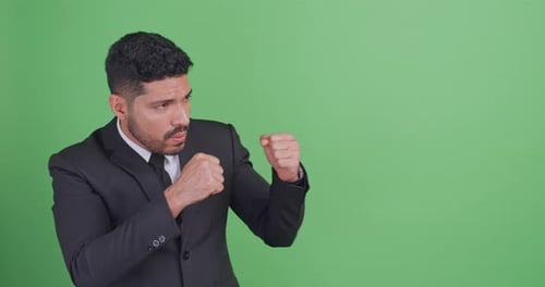 Asian businessman in a black suit is fighting for something. Isolated on green background in studio.
