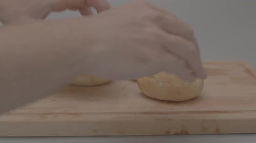 Hands placing kaiser rolls breads on a wooden plank in a studio