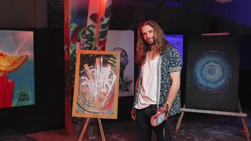 Artist Holding Palette and Standing Near Easel in Studio