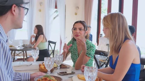 Group of diverse friend talking and eating food together in restaurant.