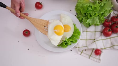 Woman Puts Fried Egg on a White Ceramic Plate with Salad