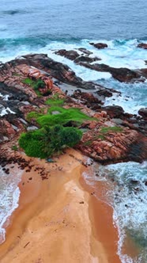Sandy beach ending with boulders washed by the waves of the ocean.