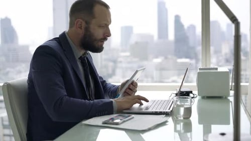 Junger Geschäftsmann arbeitet mit Tablet und Laptop im modernen Büro