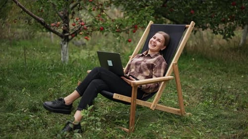 Woman Using Laptop in Orchard Sitting in Lounge Chair