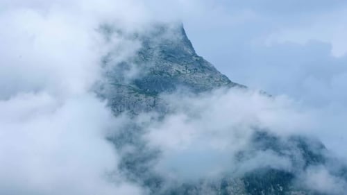 Timelapse of cloud covering blue mountain peak with tower on top